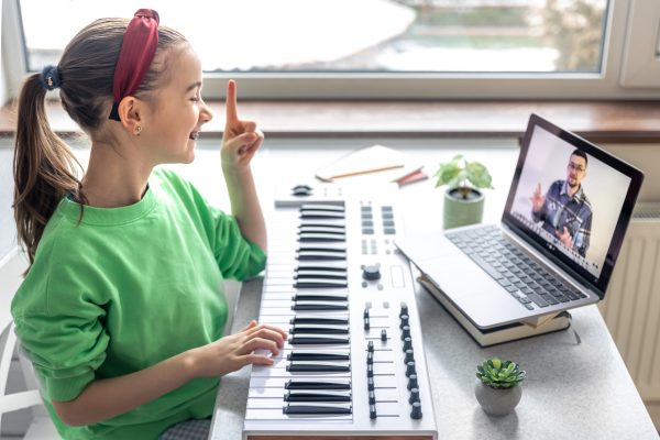 Little girl learns to play piano with teacher online, remote music learning, music lesson at home with laptop.
